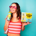Woman holding a drink and a box of 'Spiked Pop' against a teal background