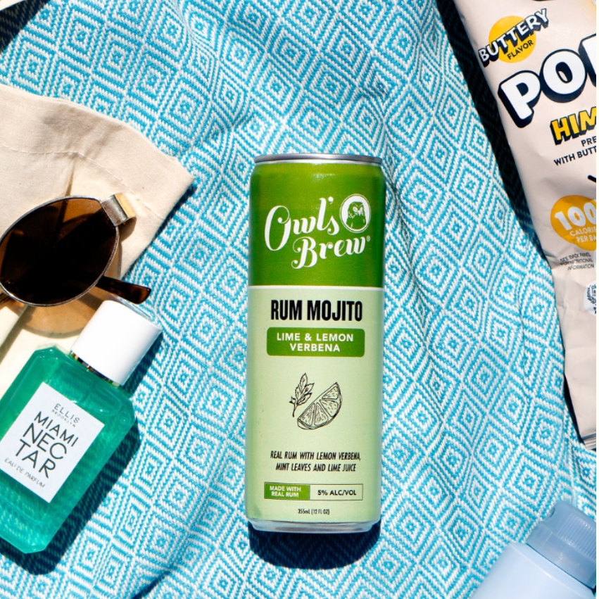 Cans of Owl's Brew Rum Mojito and Neutrogena products on a blue patterned surface.